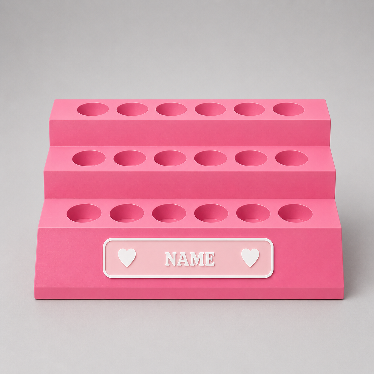 Pink three-tiered organizer with customizable name label on a gray background