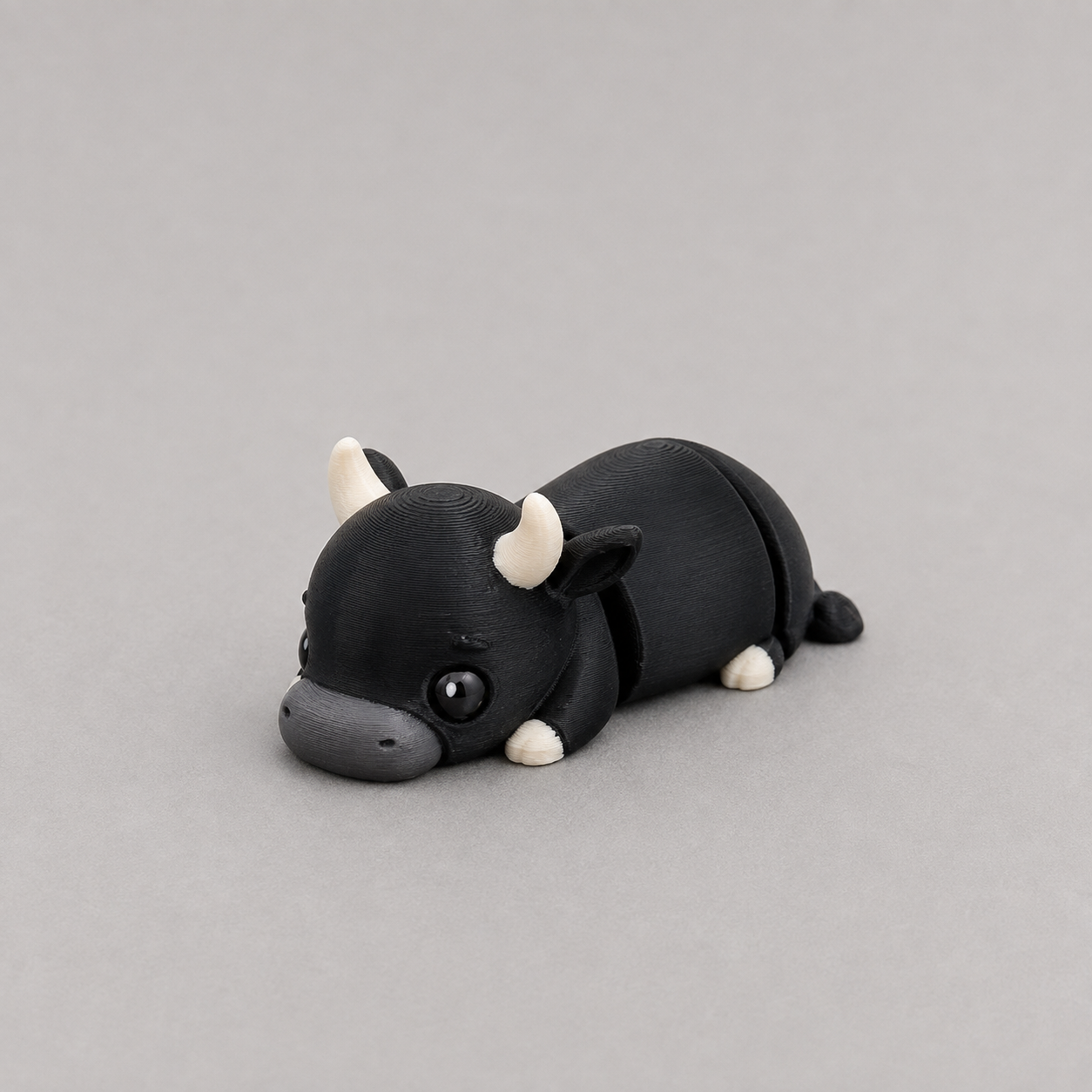 3D printed Teeny Bull figure in jet black with white horns, lying down