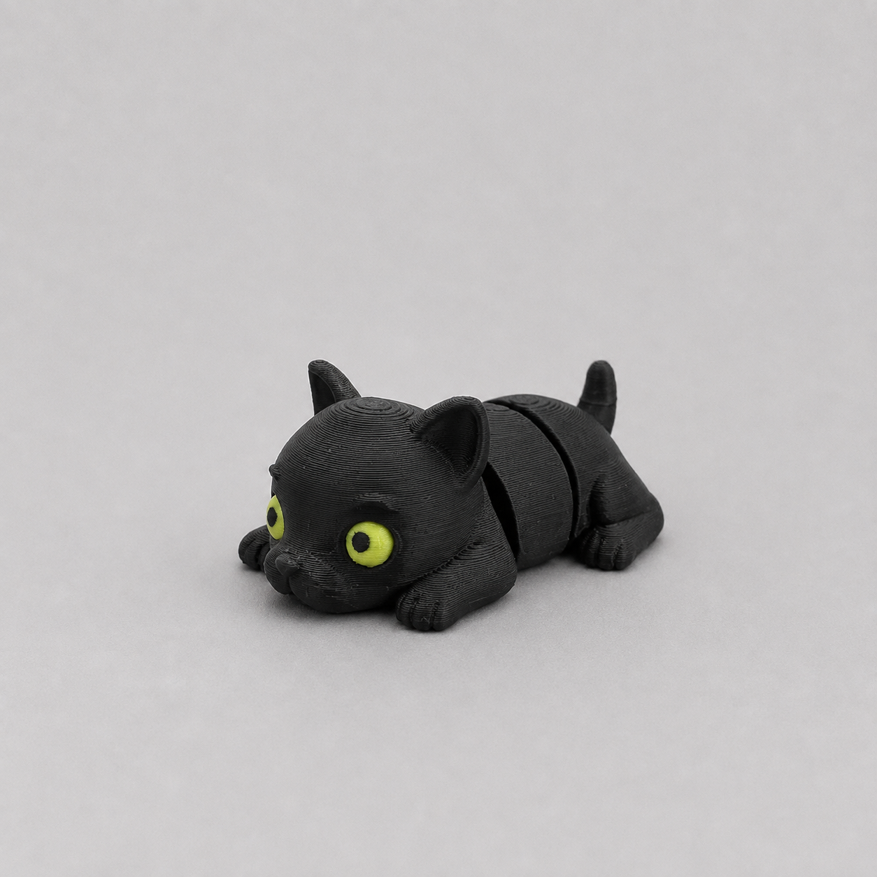 3D printed Teeny Black Panther figure in jet black with yellow-green eyes, lying down