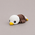 3D printed Teeny Bald Eagle figure with white head, yellow beak and brown wings, lying down