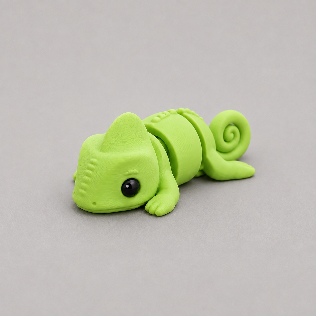 3D printed Teeny Chameleon figure in vivid lime green with curled tail, lying down
