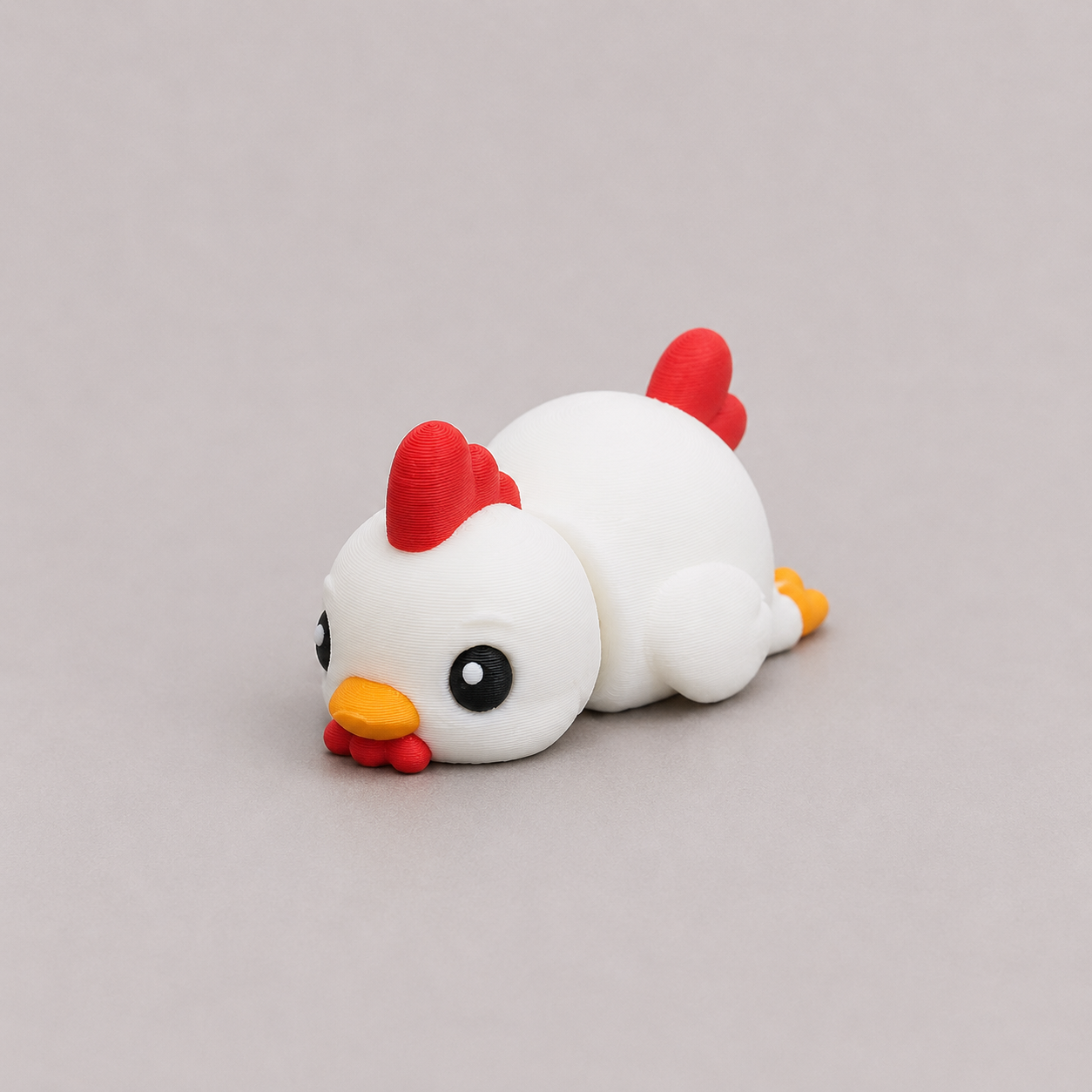 3D printed Teeny Chicken figure in white with red comb and yellow beak, lying down
