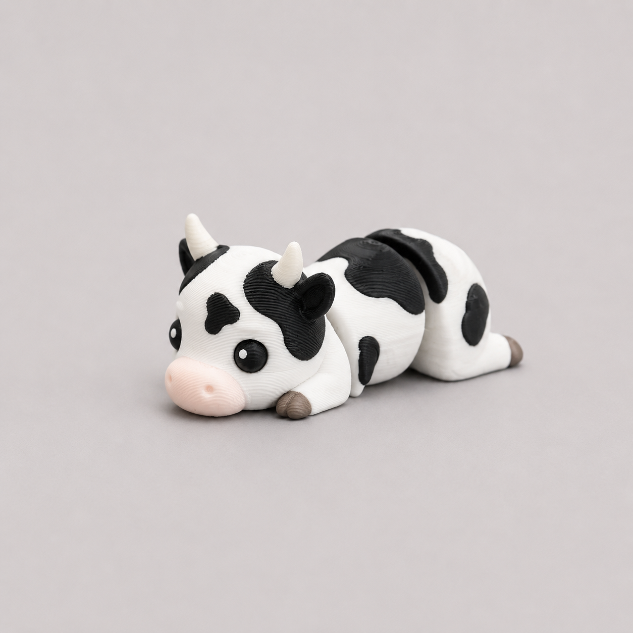 3D printed Teeny Cow figure in black and white with pink muzzle, lying down
