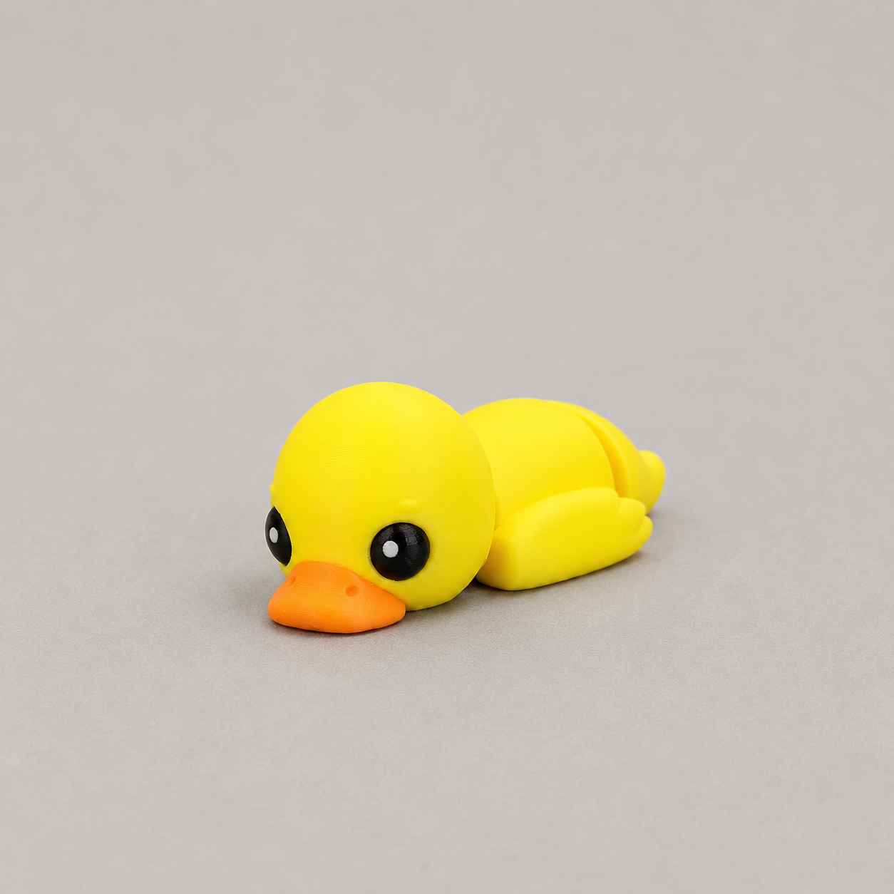 3D printed Teeny Duck figure in bright yellow with orange beak, lying down