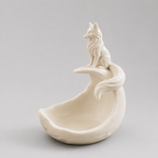 White ceramic sculpture of a wolf on a crescent moon against a gray background