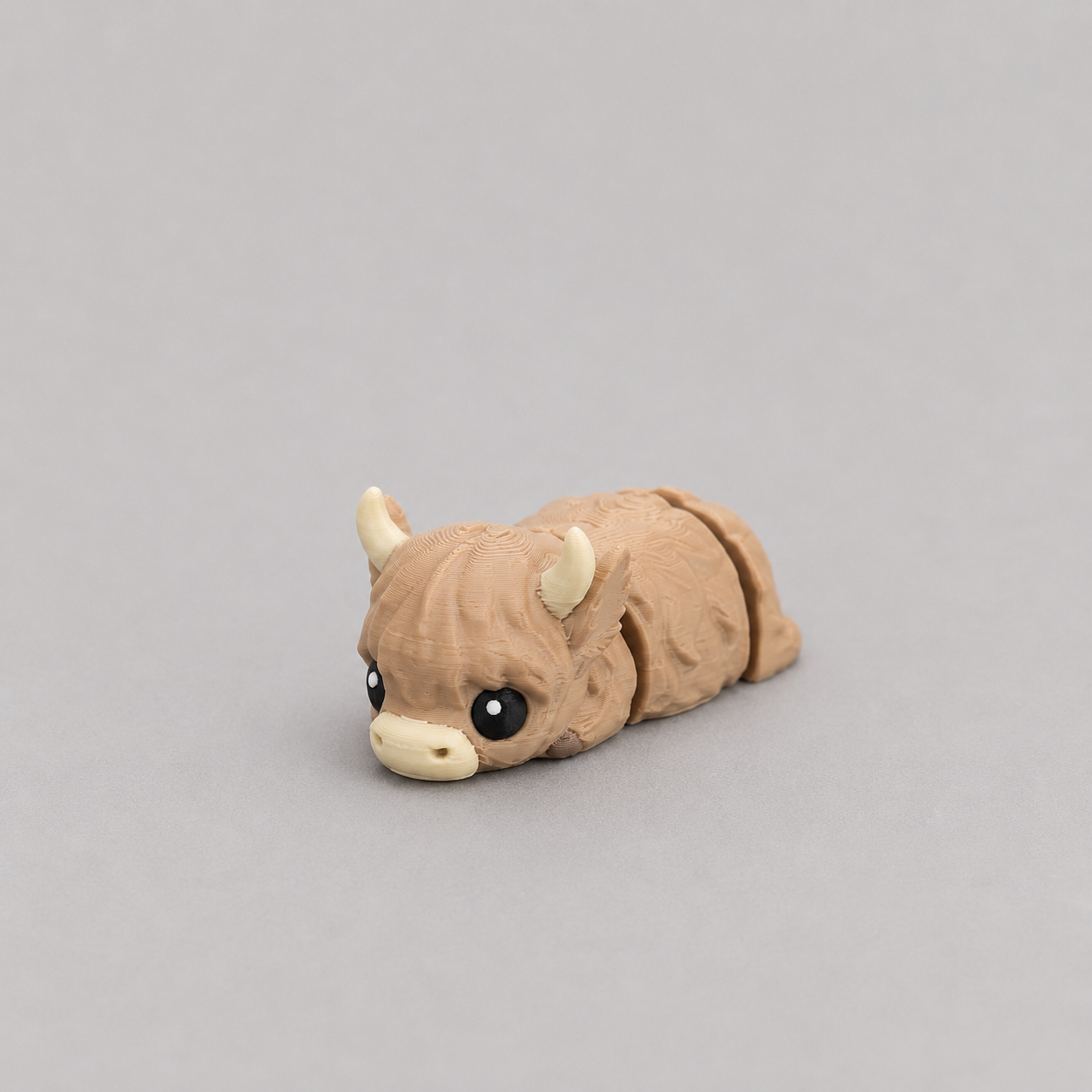 3D printed Teeny Highland Cow figure in warm brown with cream horns, lying down