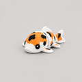 3D printed Teeny Koi Carp figure in white with orange and black patches, lying down