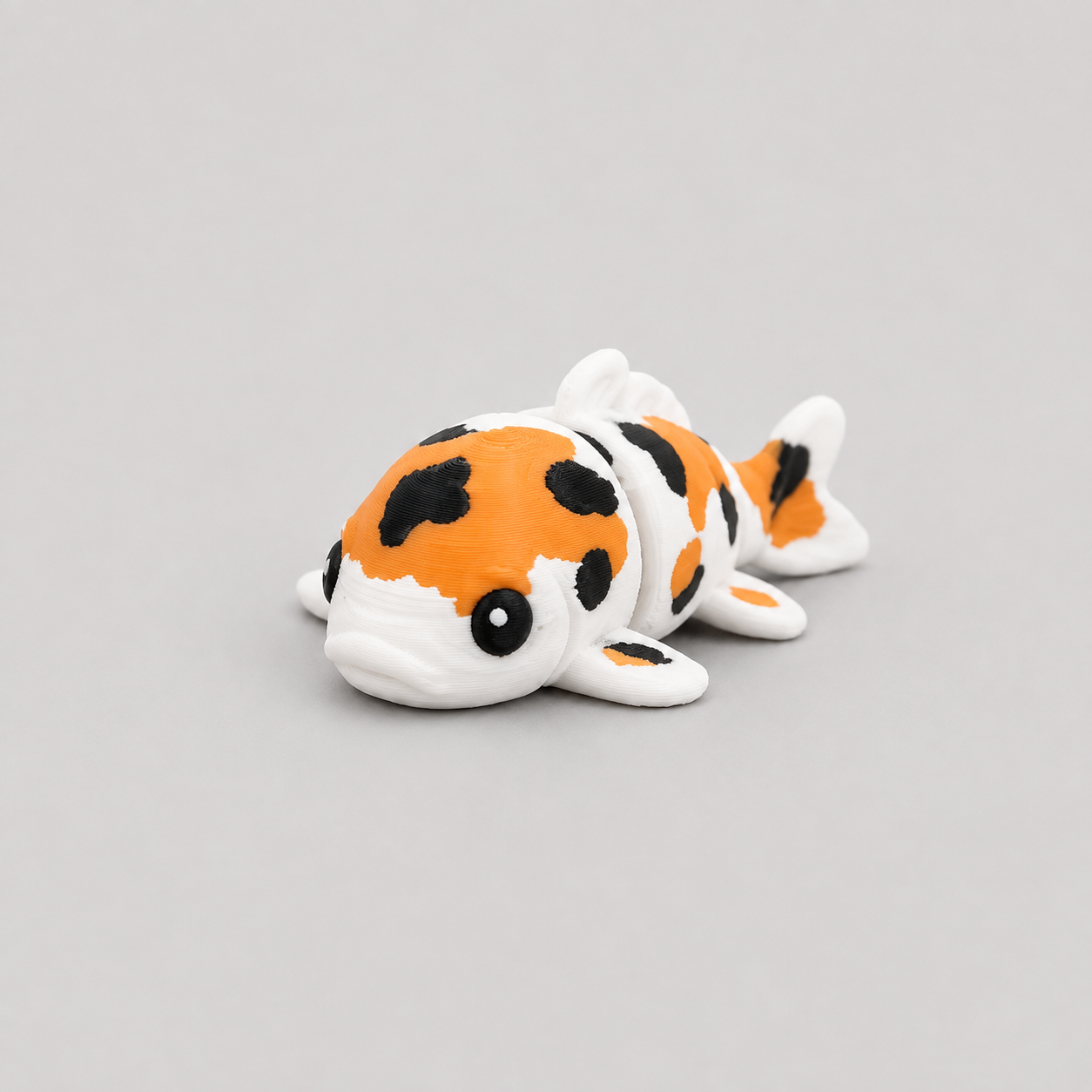 3D printed Teeny Koi Carp figure in white with orange and black patches, lying down