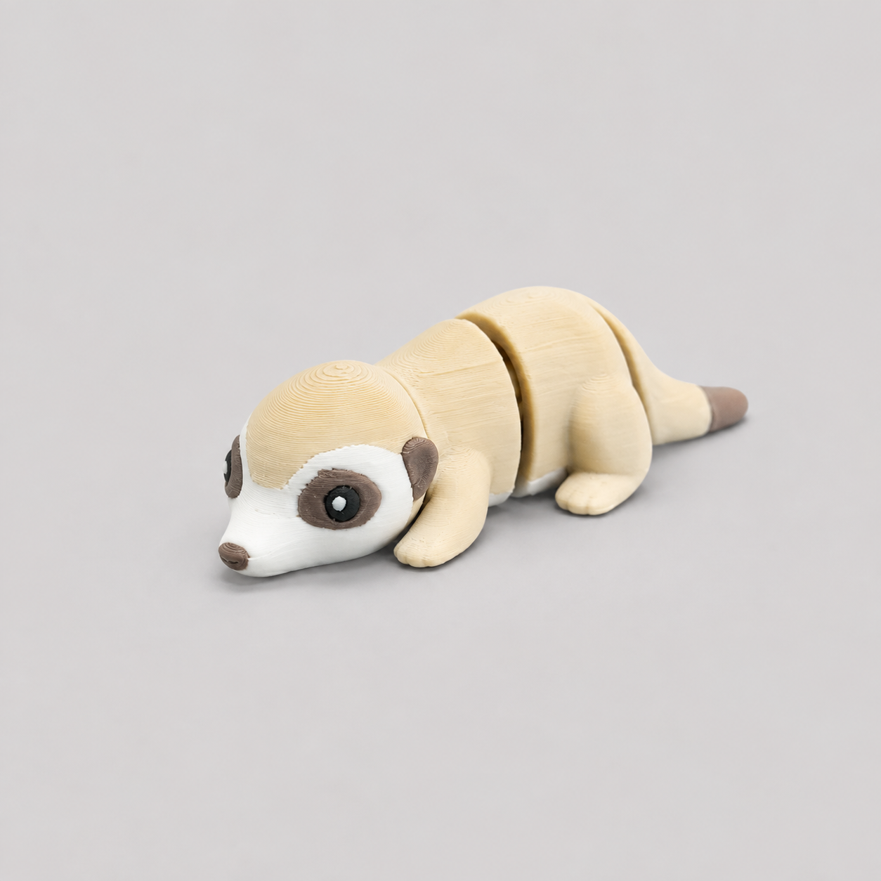 3D printed Teeny Meerkat figure in sandy beige with white face and dark eye patches, lying down