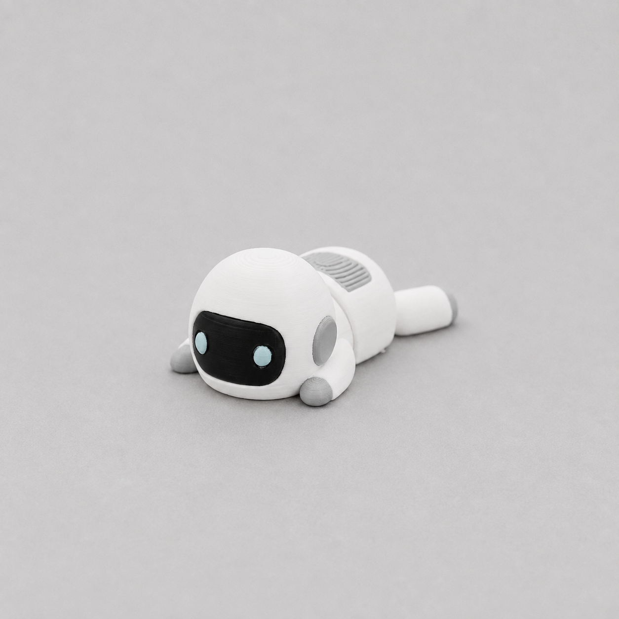 3D printed Teeny Robot figure in white with black visor and blue eyes, lying down