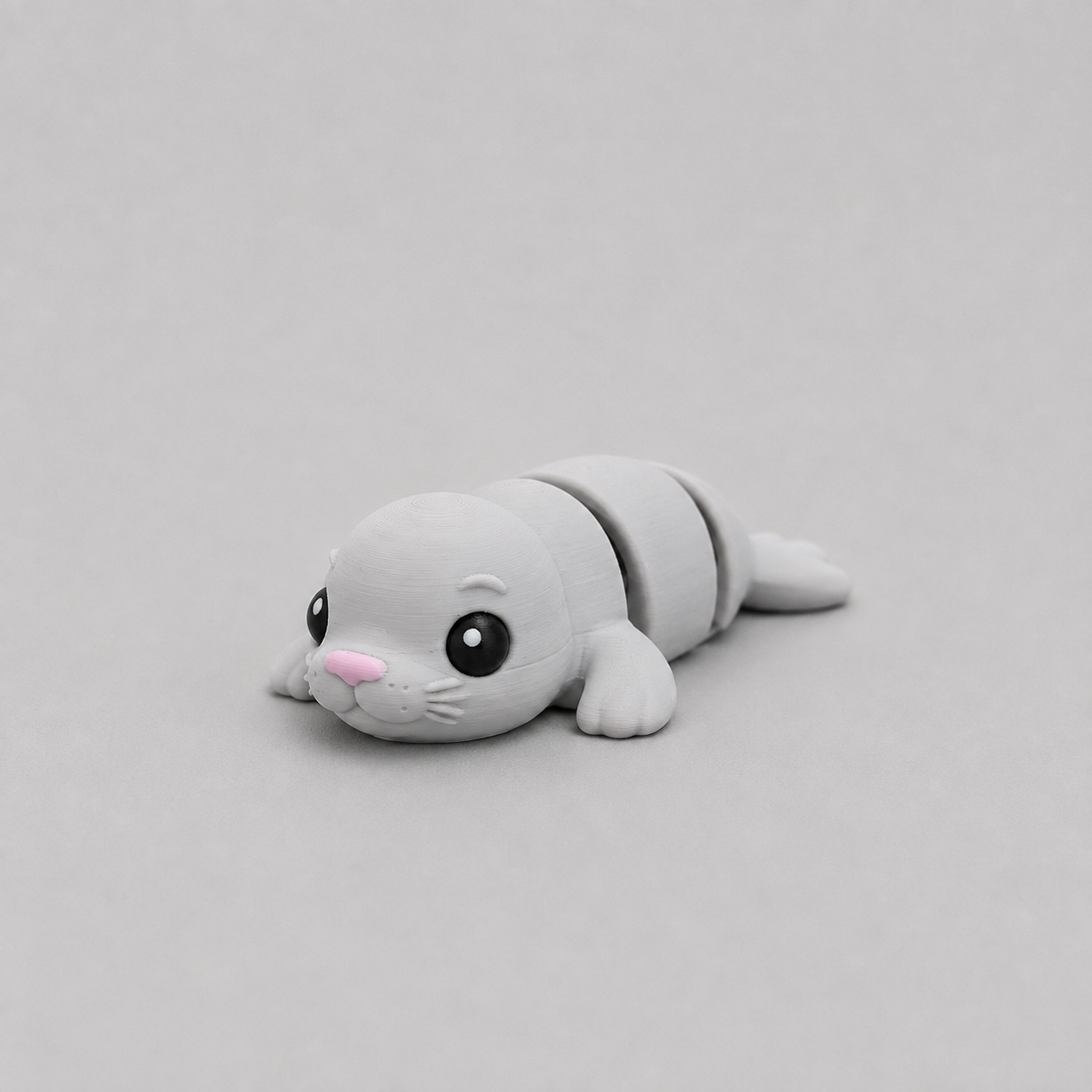 3D printed Teeny Seal figure in soft grey with pink nose, lying down