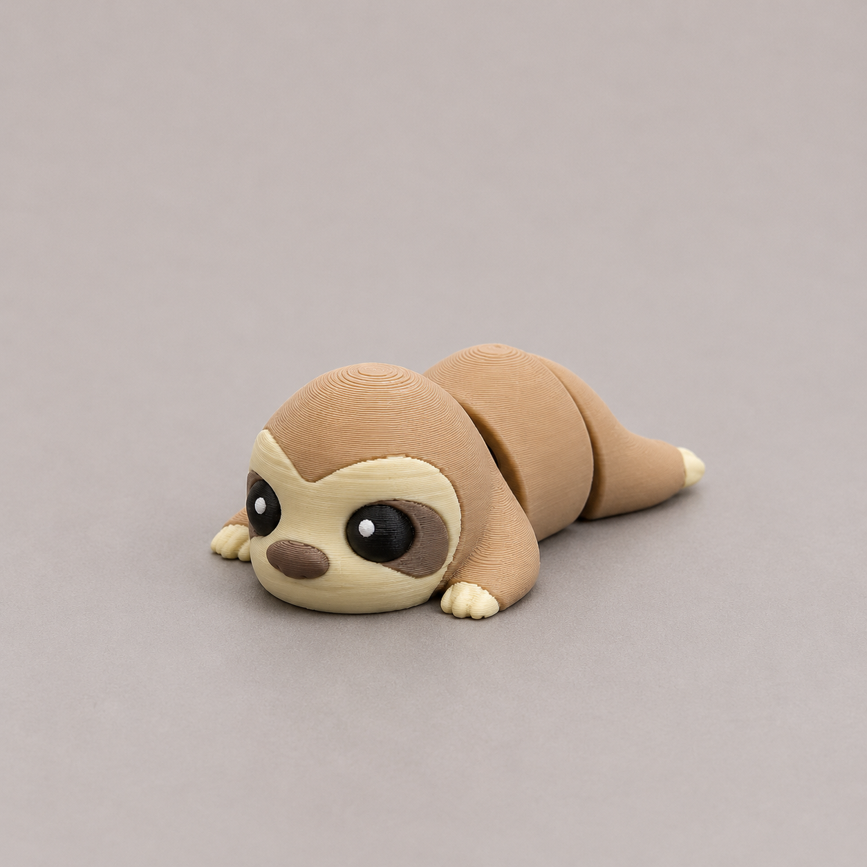 3D printed Teeny Sloth figure in warm sandy beige with cream face, lying down
