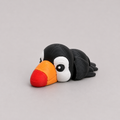 3D printed Teeny Toucan figure in jet black with bold orange and red beak, lying down
